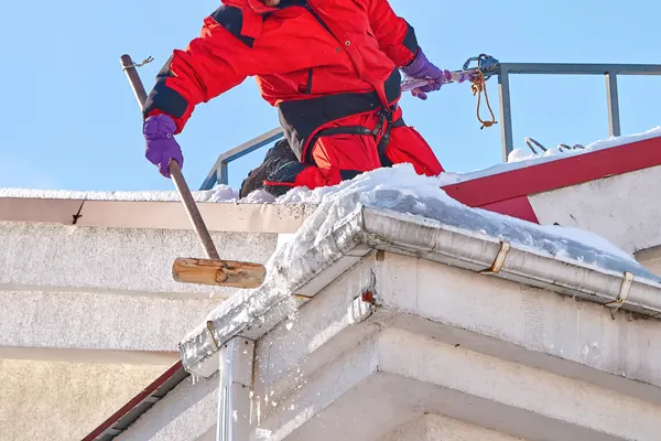 Alpinista zbija lód i śnieg z krawędzi dachu